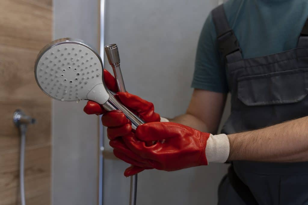 Un homme entrain de réparer ou d'installer un pommeau dans une douche